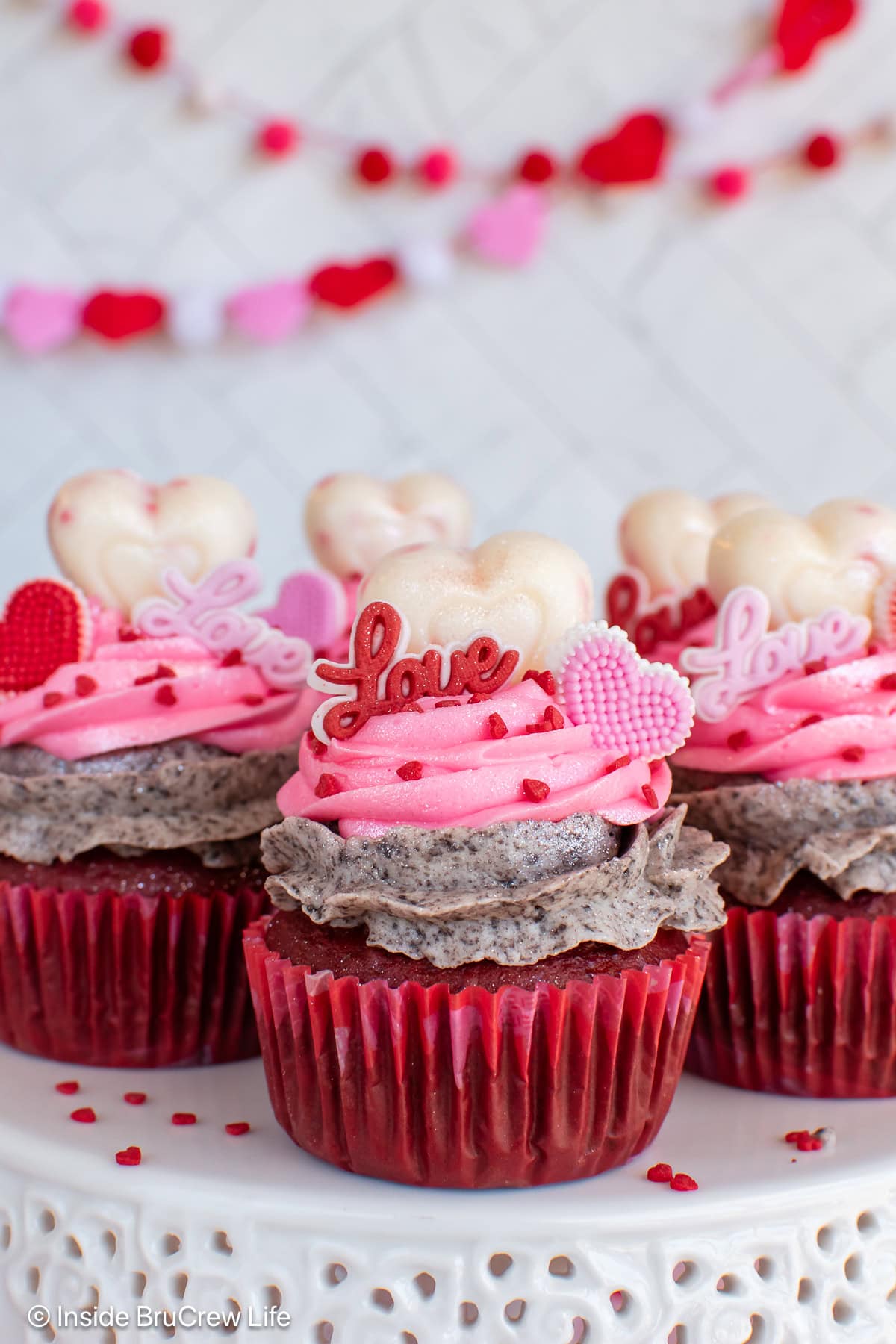 Pink and Oreo frosting on top of red velvet cupcakes on a white tray.