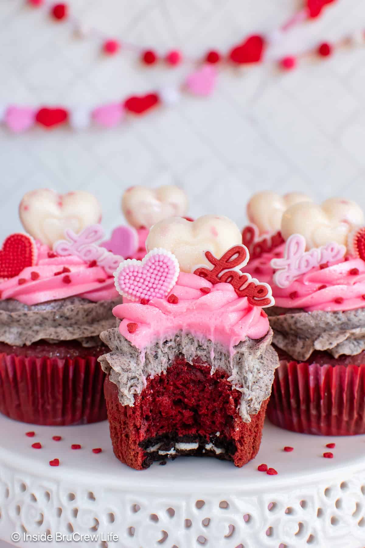 Frosted red velvet cupcakes with a bite out of one showing the hidden Oreo.