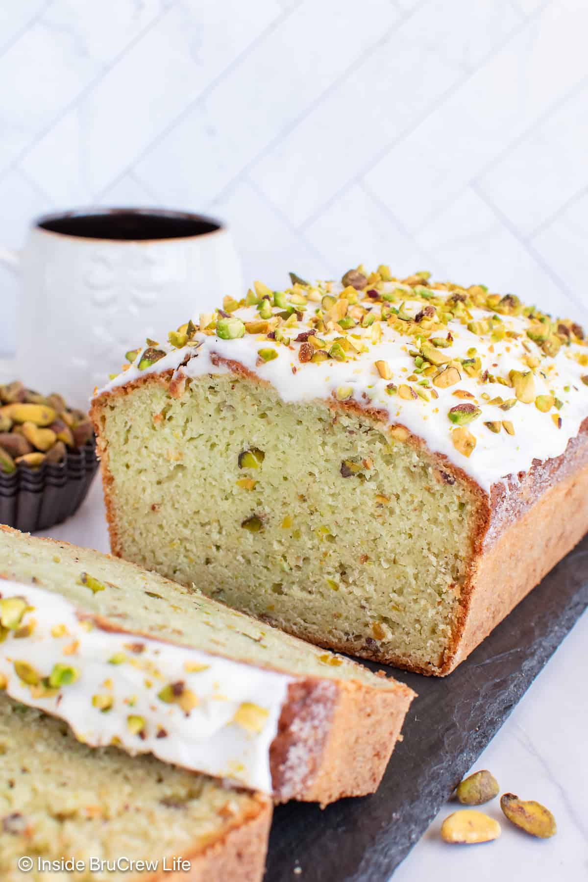 A loaf of frosted pistachio pudding bread on a tray.