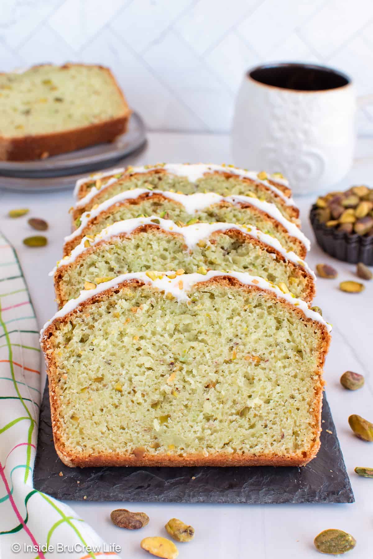 Slices of a pistachio loaf laying on a black tray.