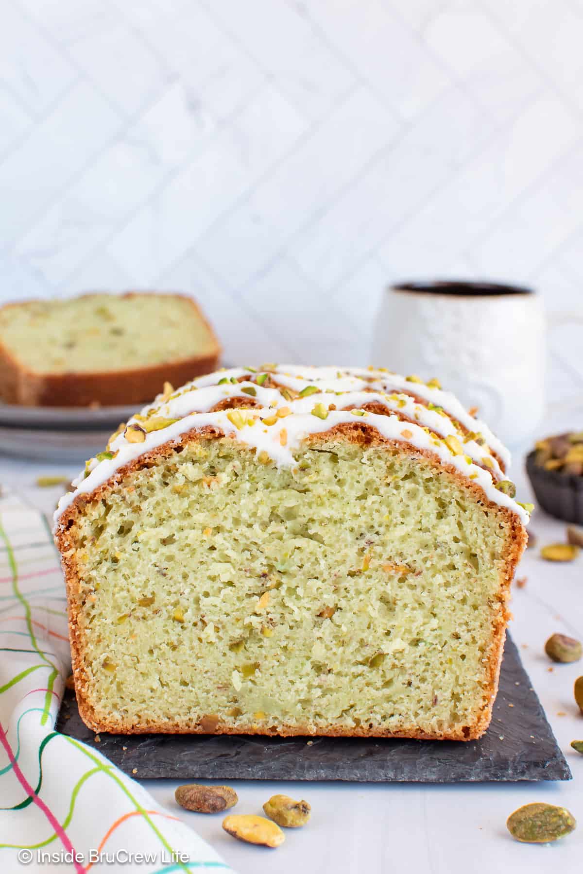 A sliced loaf of pistachio bread standing on a slate board.