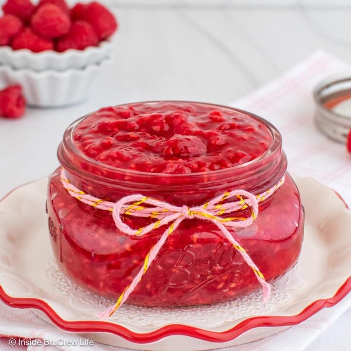 A glass jar filled with homemade raspberry pie filling sitting on a plate.