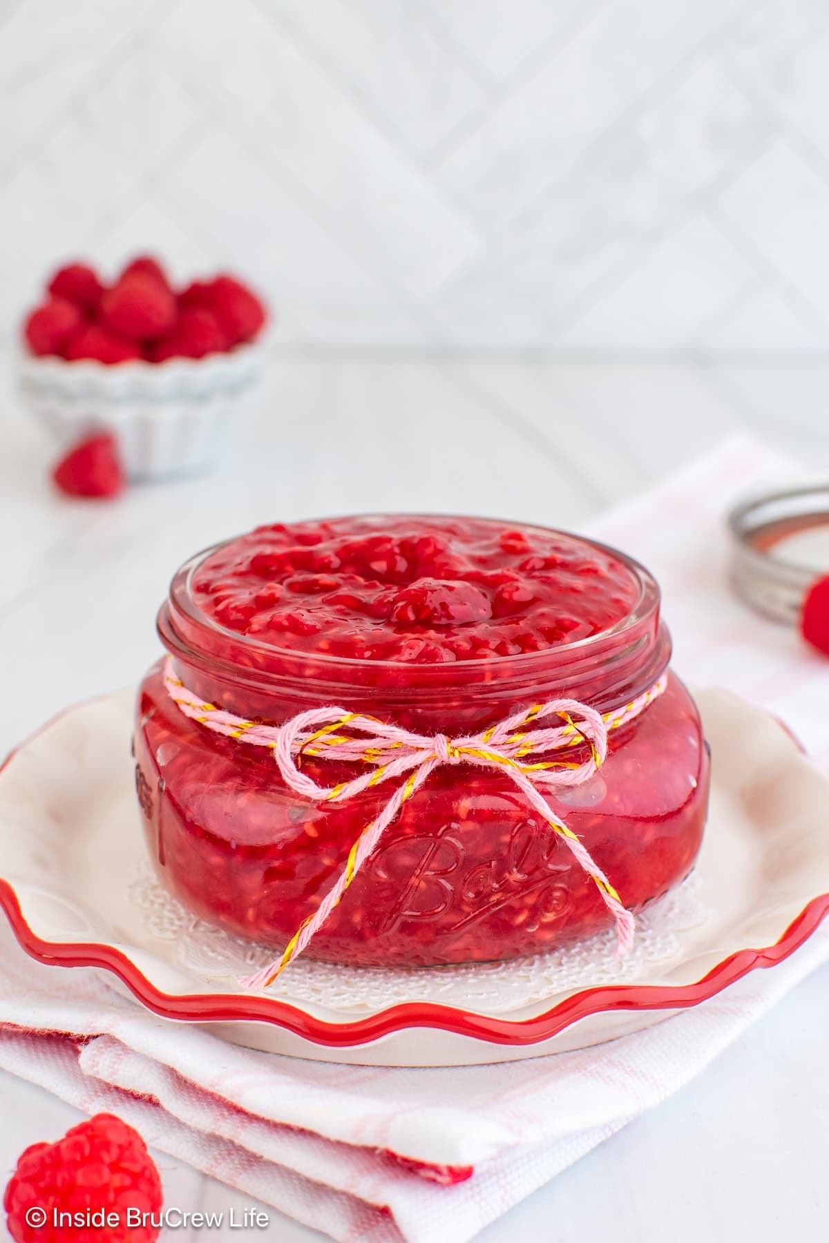 A glass jar filled with homemade raspberry pie filling sitting on a plate.