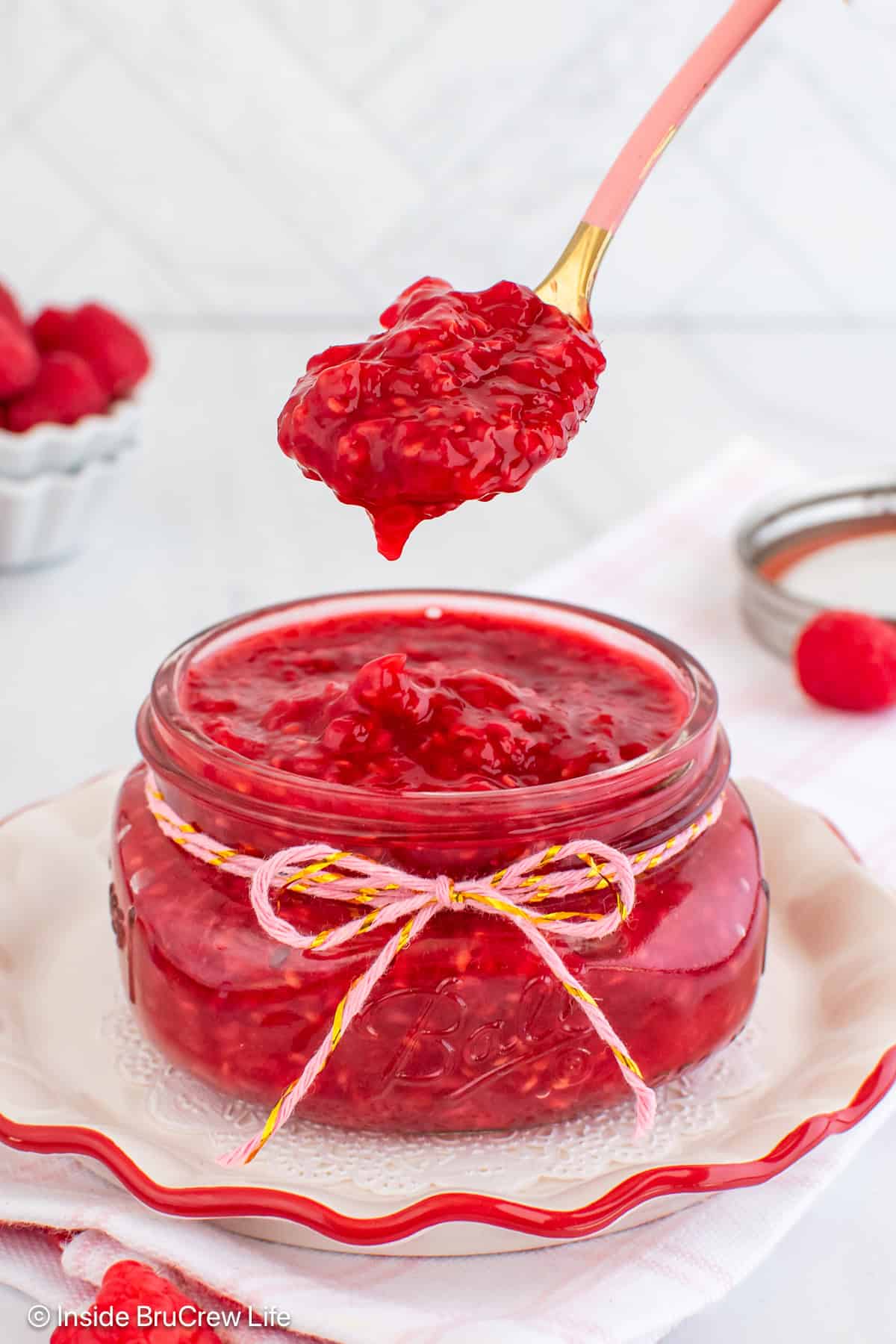 A glass jar filled with raspberry pie filling with a spoon lifting out a spoonful of filling.
