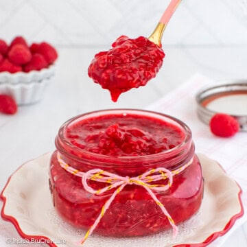 A glass jar filled with raspberry pie filling with a spoon lifting out a spoonful of filling.