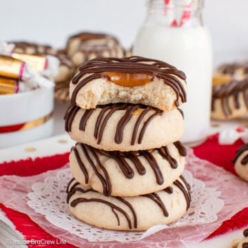 A stack of chocolate drizzled Twix cookies on a white doily.