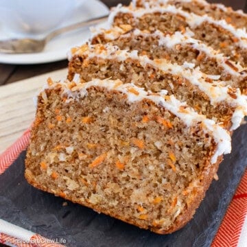 Slices of frosted carrot cake bread laying on a black tray.
