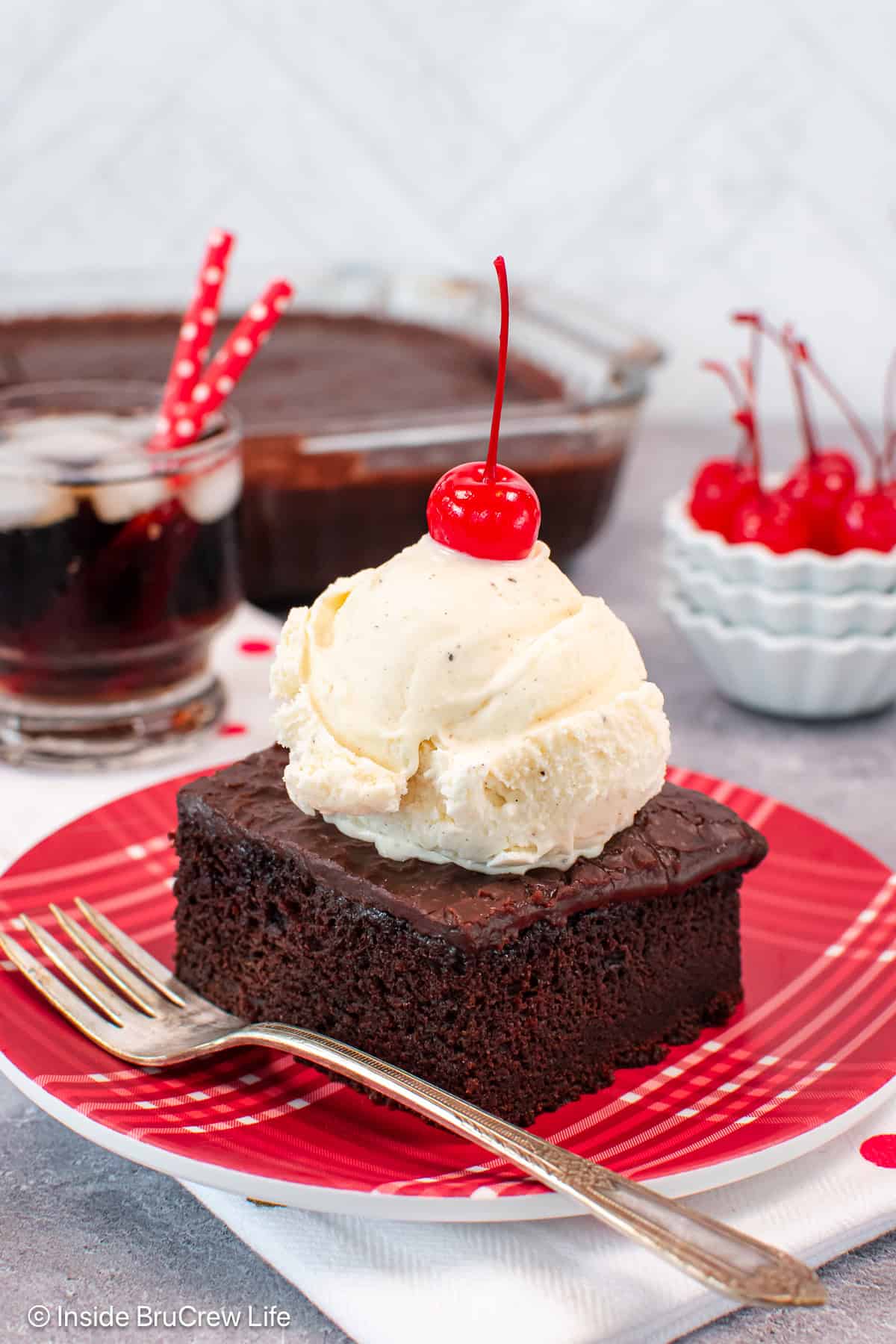 A piece of coca cola cake topped with a scoop of ice cream and a cherry.