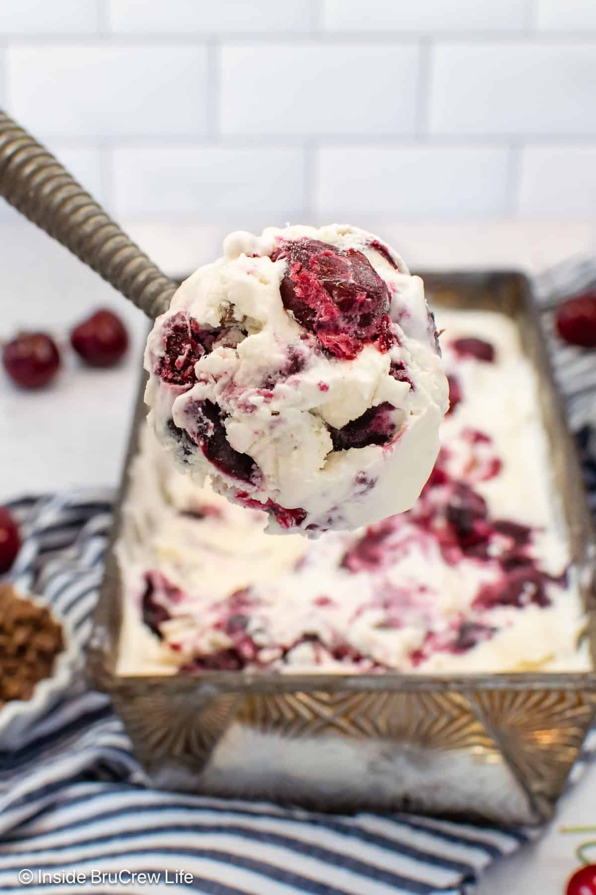 A scoop of cherry vanilla ice being lifted out of a container on a scoop.