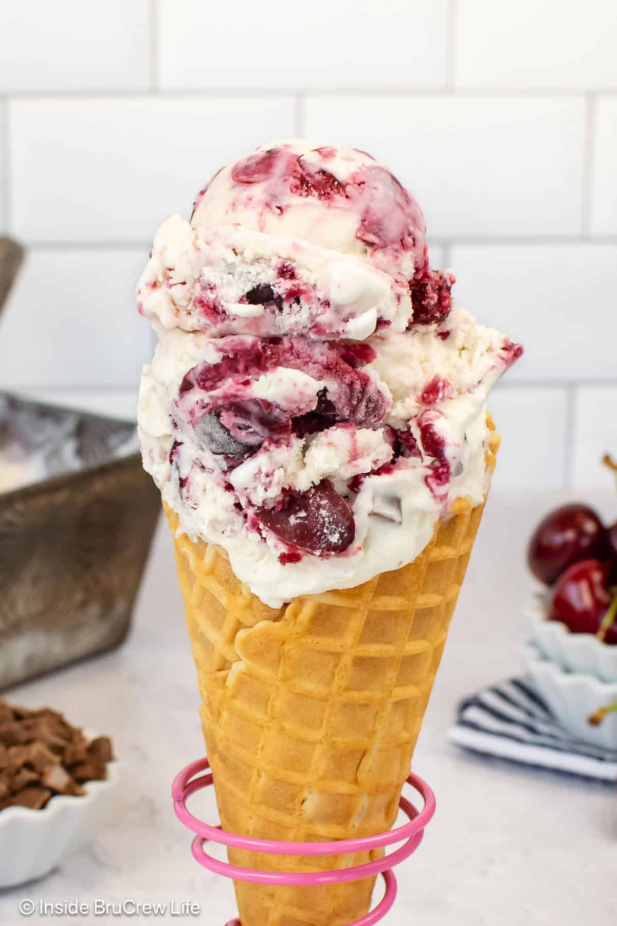 A close up of a waffle cone filled with scoops of cherry vanilla ice cream.