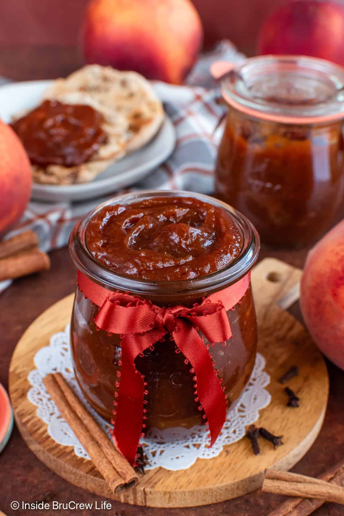 Two jars of homemade peach butter and an English muffin with spread on it.