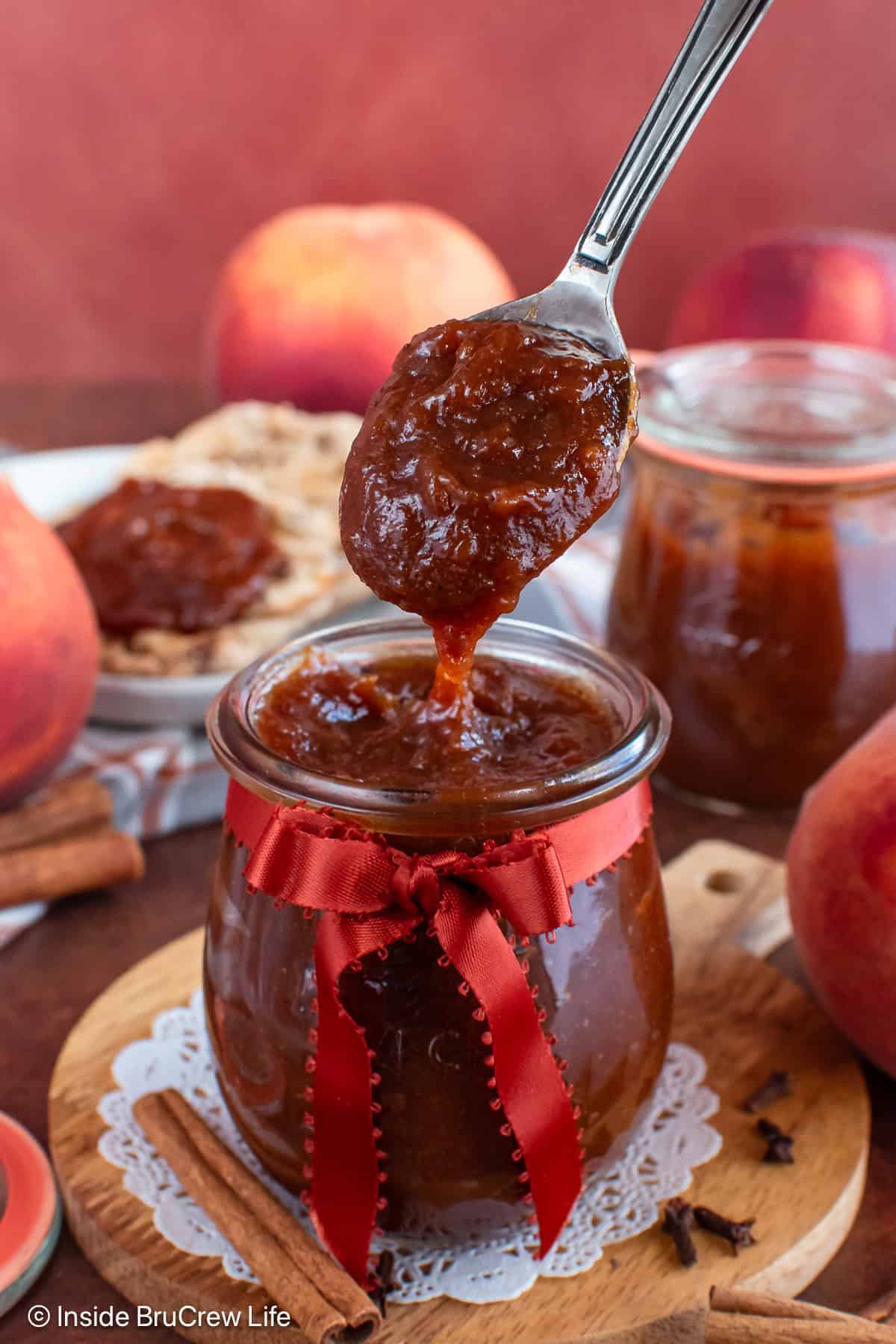 A jar of peach butter with a spoon lifting it out.