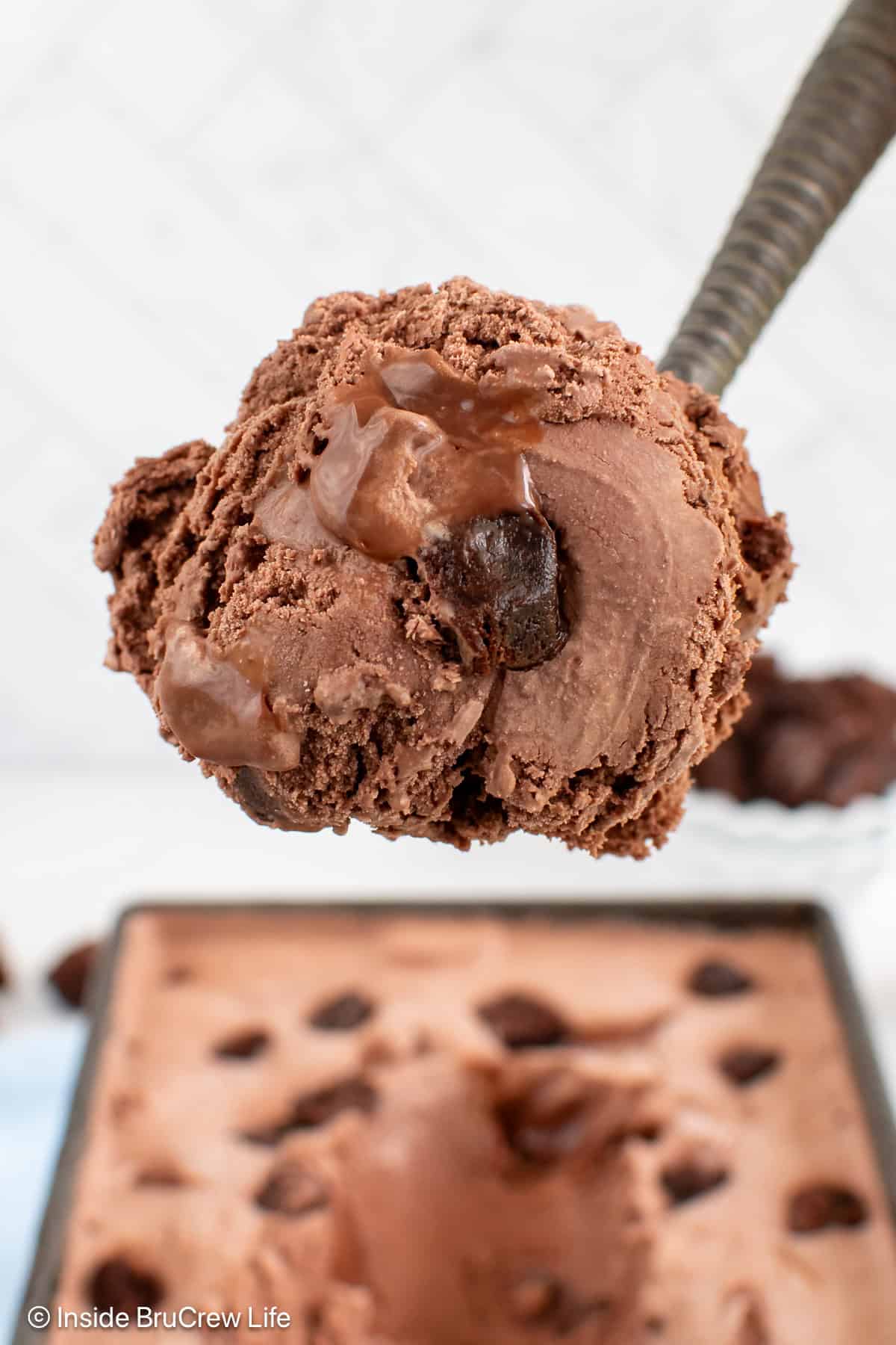 A scoop of chocolate fudge brownie ice cream being lifted out of the container.