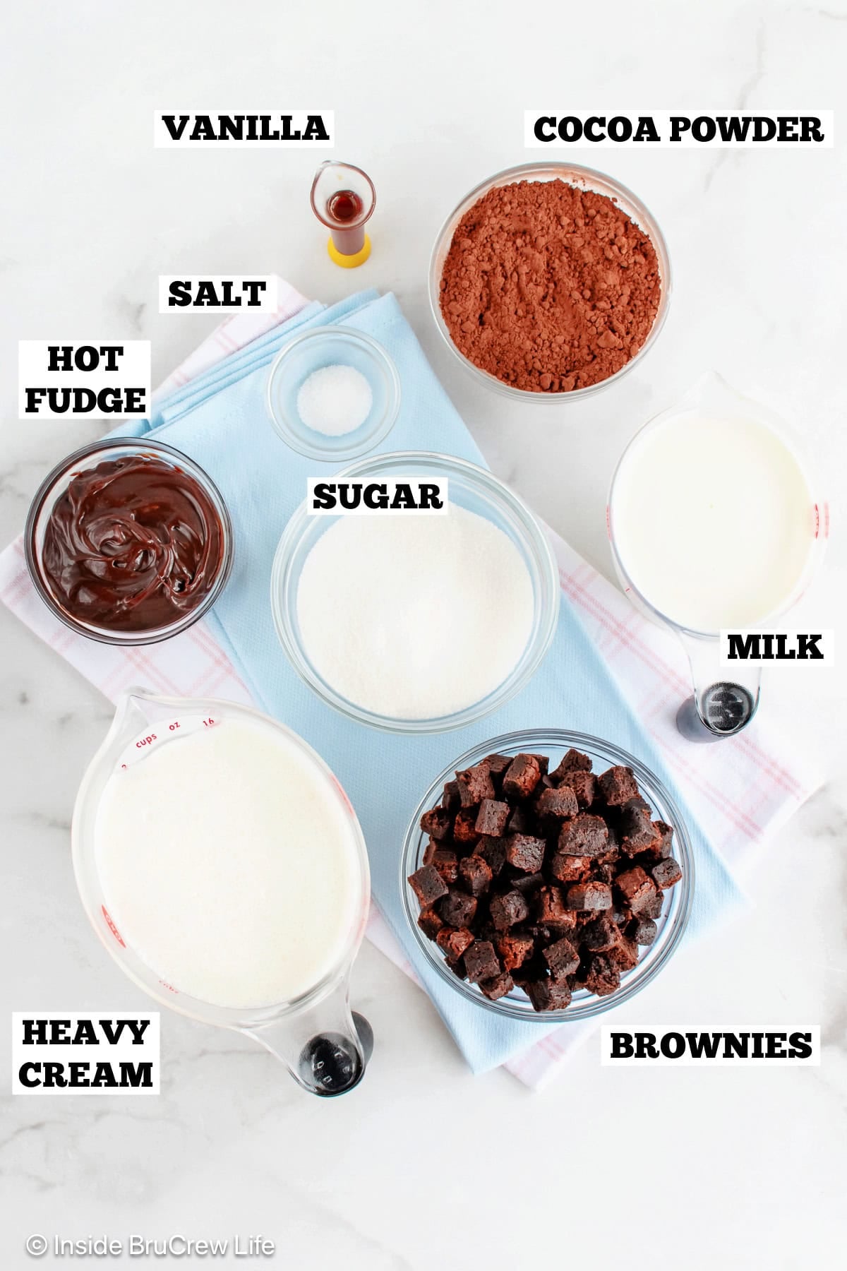 Ingredients for a homemade chocolate fudge brownie ice cream on a white board.