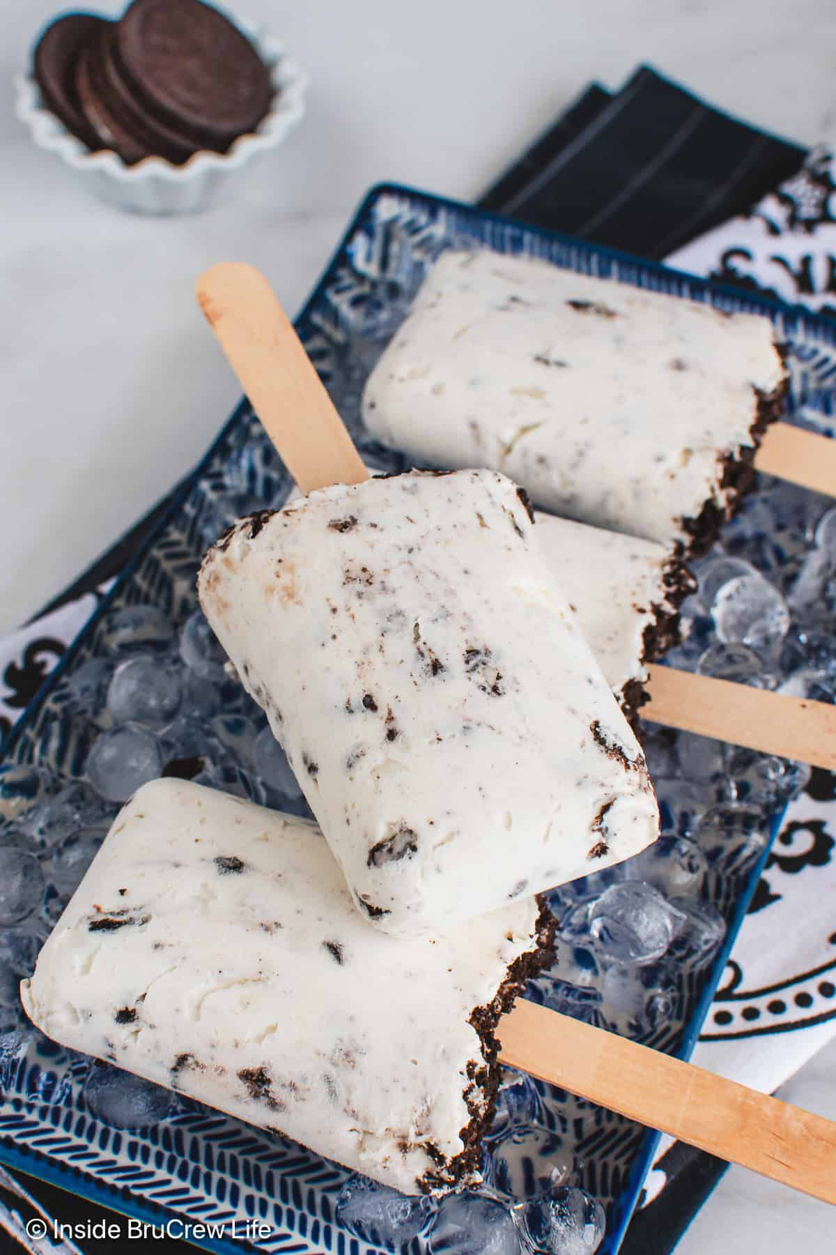 A blue plate with four cookies and cream popsicles on ice.