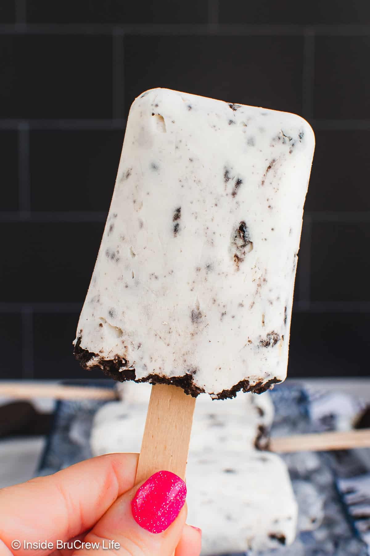 A hand holding up a cookies and cream popsicle.