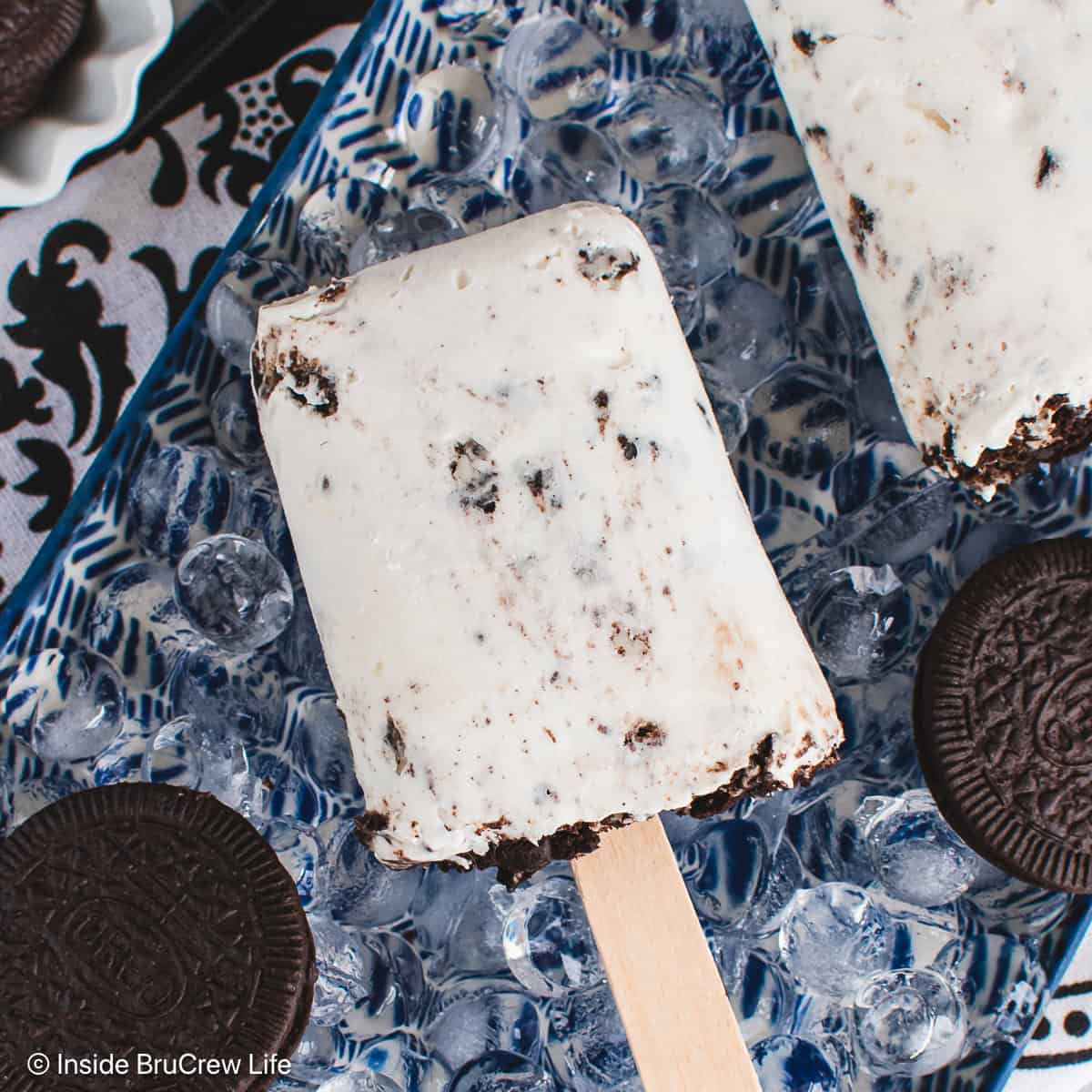 Two yogurt cookies and cream popsicles on a plate of ice.