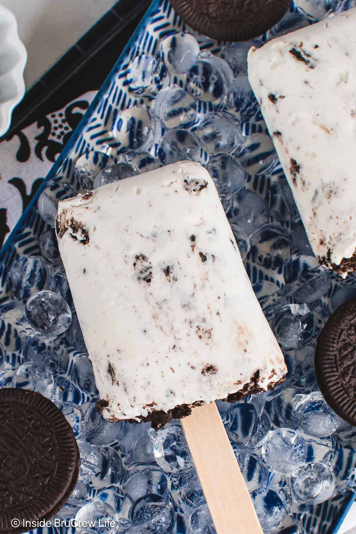 Two yogurt cookies and cream popsicles on a plate of ice.