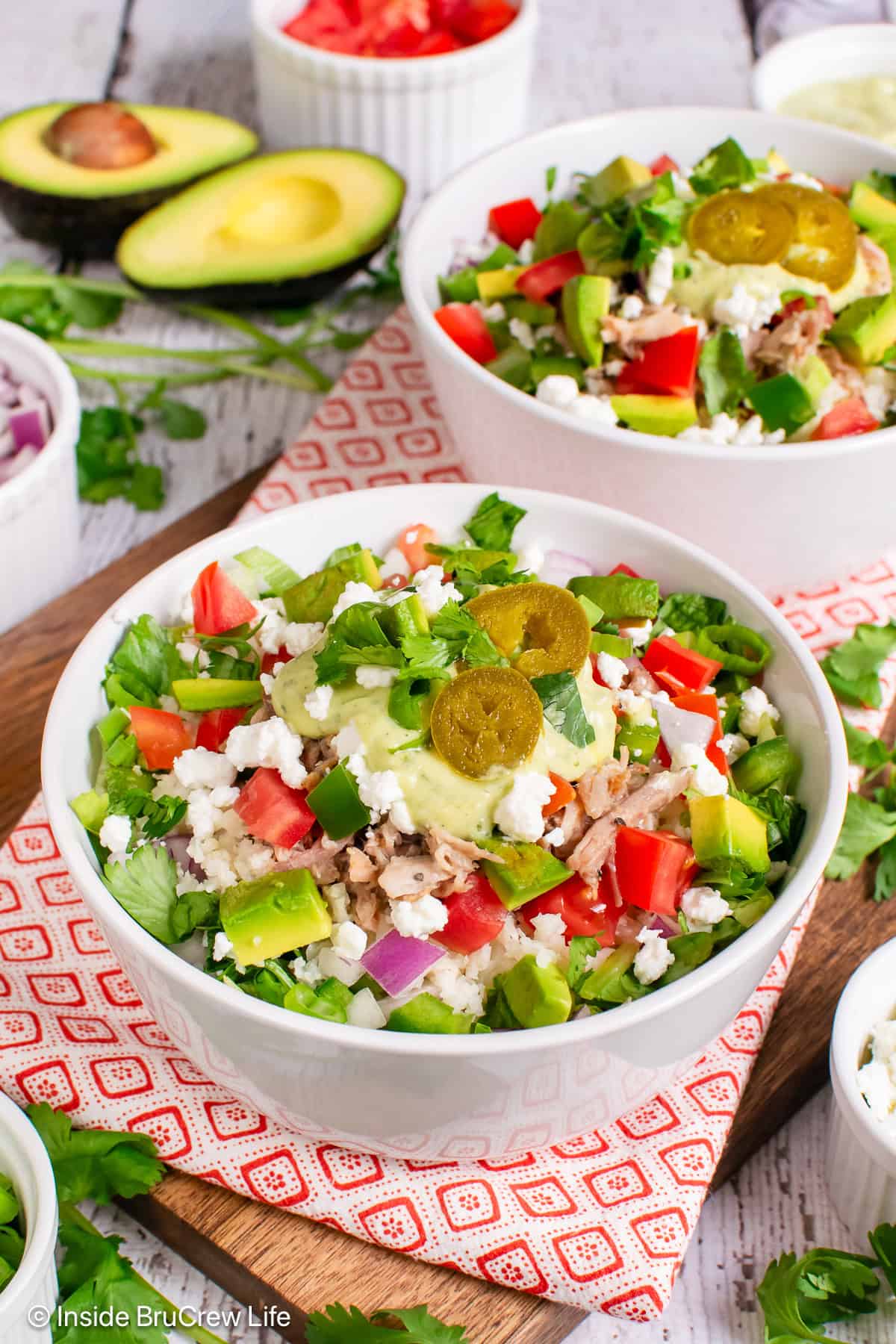 A pork burrito bowl piled with meat, veggies, cheese, and dressing.