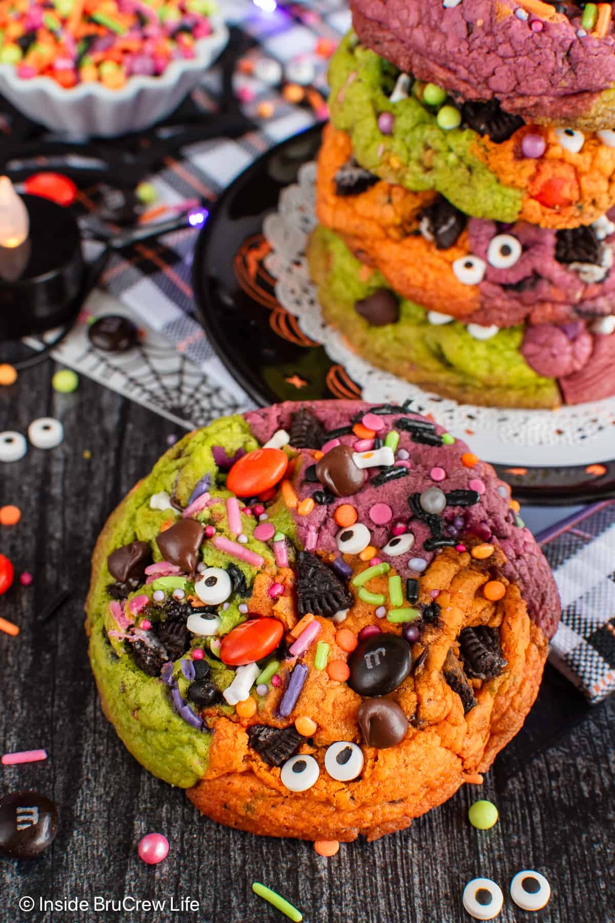 A stack of colorful Halloween chocolate chip cookies with one sitting beside it.