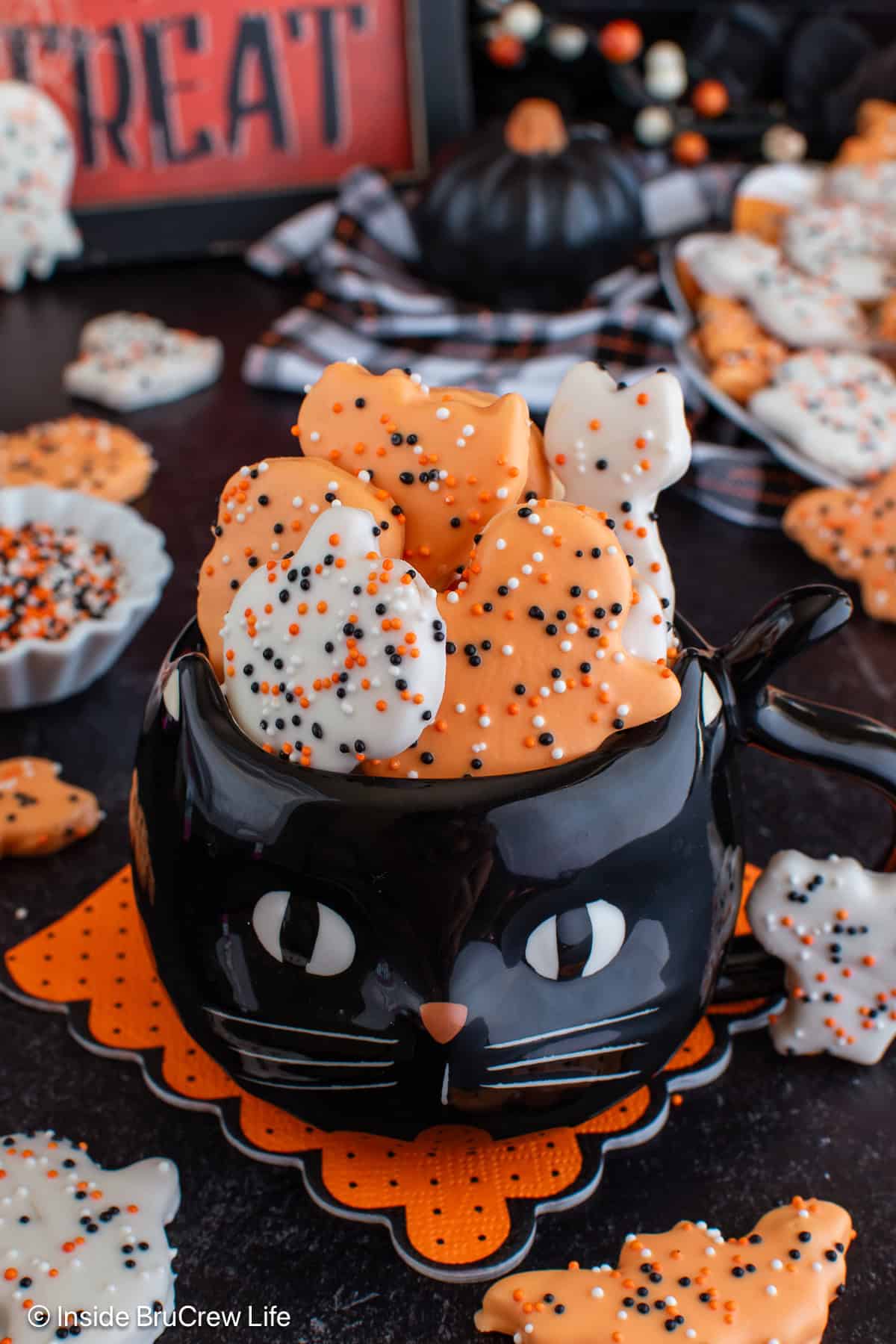 A black cat cup filled with orange and white frosted animal cookies.
